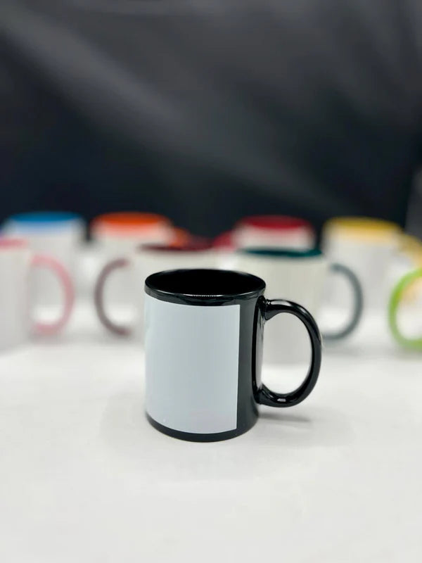 Black mug with a white interior on a white surface with blurred colorful mugs in the background.