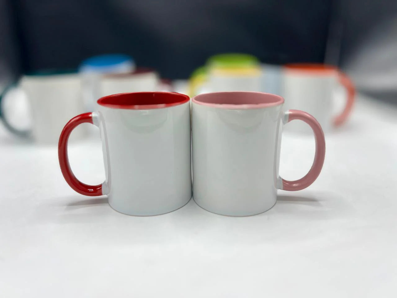 Two mugs with red interior and handles on a white surface.