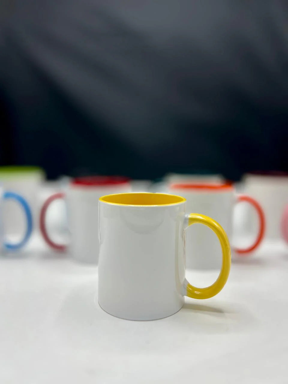 White mug with a yellow handle on a white surface, with blurred background