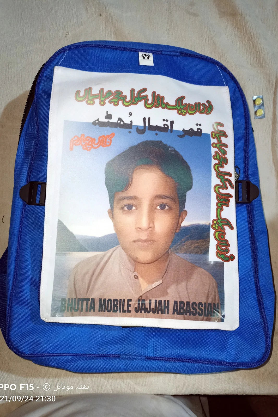 Blue backpack with a printed photo of a young boy on a beige surface