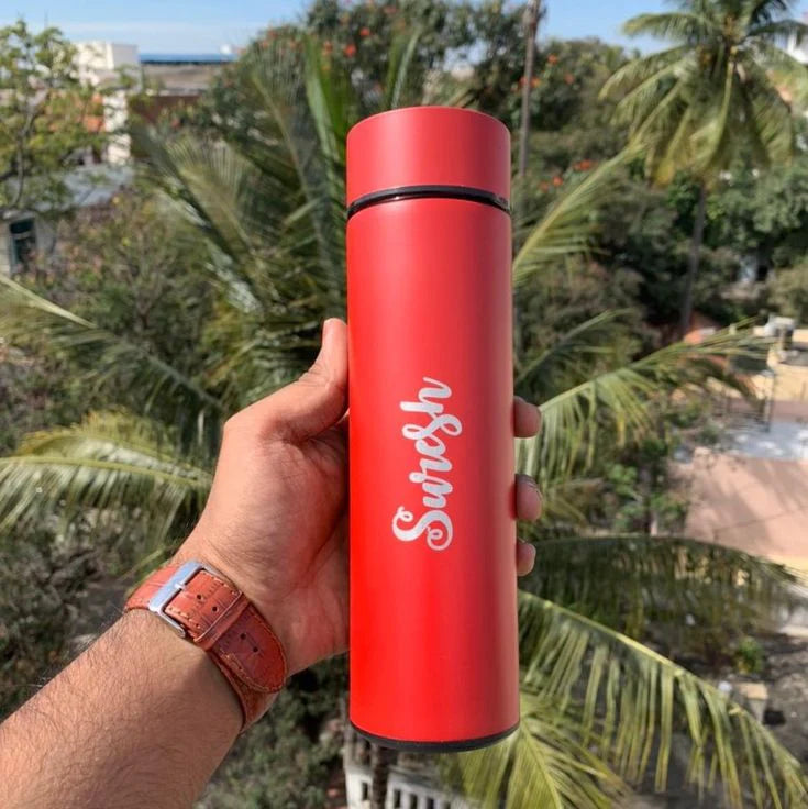 Red thermos with 'Swish' branding held in front of palm trees
